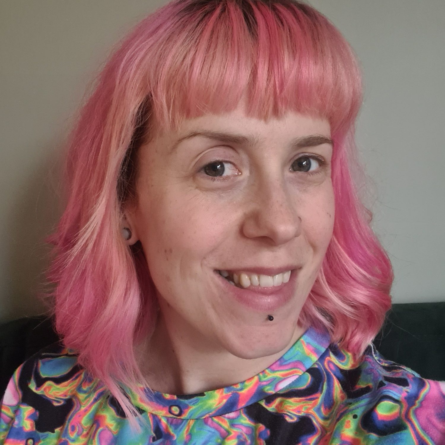 A photo of Bryony, she has pastel orange and pin hair, in a long bob with a fringe. She is looking to the camera and smiling.